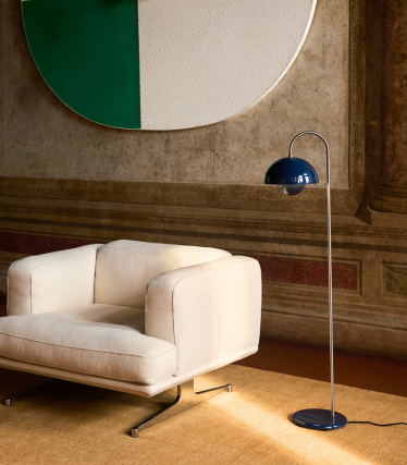 Elegant &Tradition golvlampa bredvid modern loungestol i varm interiör.