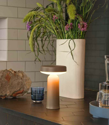 Bärbar Muuto bordslampa på mörk köksbänk med blomsterdekoration.