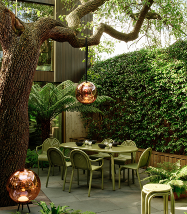Tom Dixon utomhuslampor i stilfull trädgård med matplats under gammalt träd.
