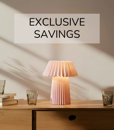 Ljusrosa bordslampa på en skänk i trä, omgiven av glas och böcker i det varma solljuset.