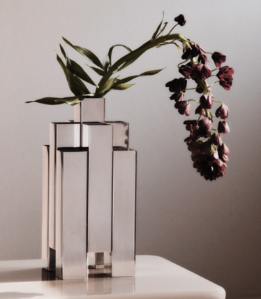 Skulptural vas i polerat rostfritt stål från Ferm Living med mörkröda blommor