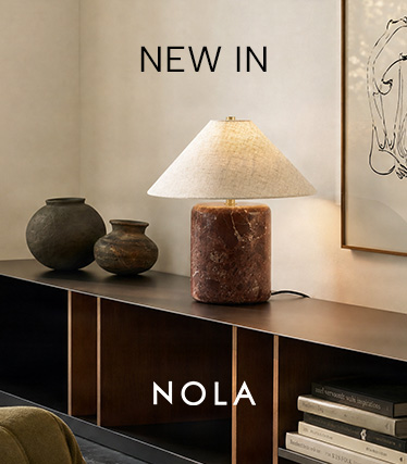 Nola-bordslampa med rödbrun marmorfot och konisk linneskärm på en mörk skänk. Text: ”Nyhet – Nola”.